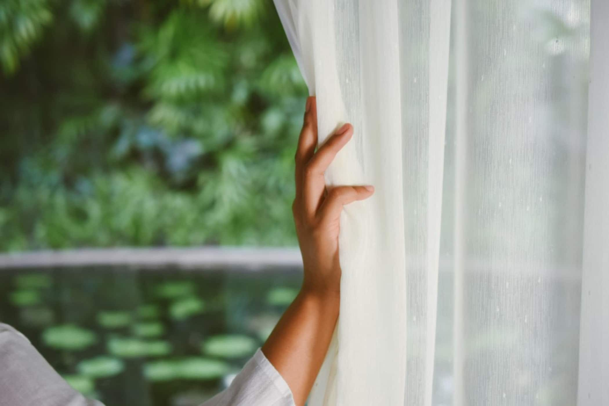 Person drawing sheer curtain with hand