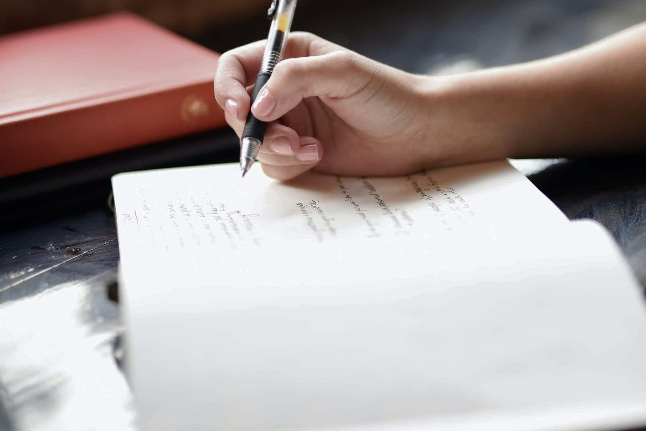 Person holding black pen ready to write on a page of a notebook