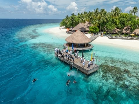 A group of people on a dock on a beach with blue water and white sands at Dhawa Ihuru in the Maldives