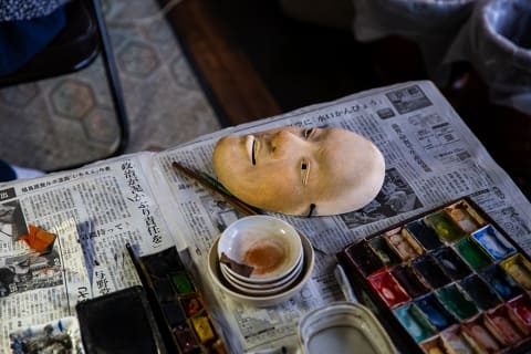 banyan tree higashiyama kyoto traditional noh mask made of wood, placed on top of newspaper next to paint colour palette