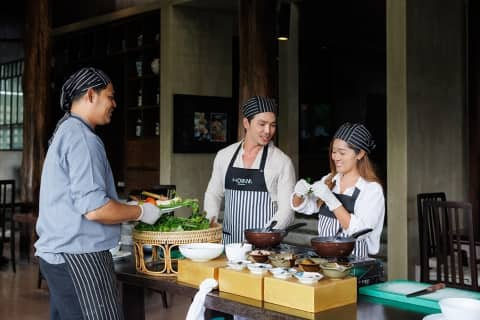 A couple wearing aprons learning how to prepare dishes at Homm Chura Samui's Coconut Cooking class