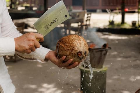 coconut husk being cracked open with a chopper, with coconut water spilling out