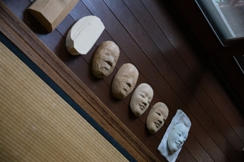 A row of carved wooden masks at a noh mask craftsman's studio in kyoto japan