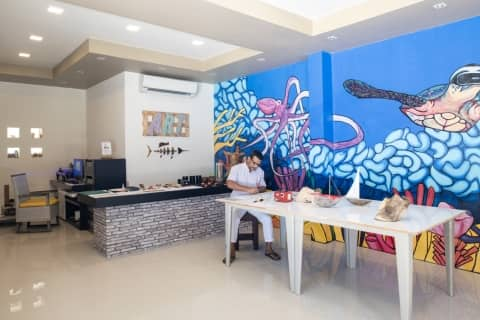 Abdulla, the in-house artist of Dhawa Ihuru in the Maldives, sitting at a table in a room with a mural