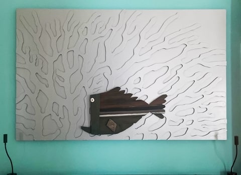 A decorative headboard of a fish swimming amongst coral reefs, made from repurposed materials.